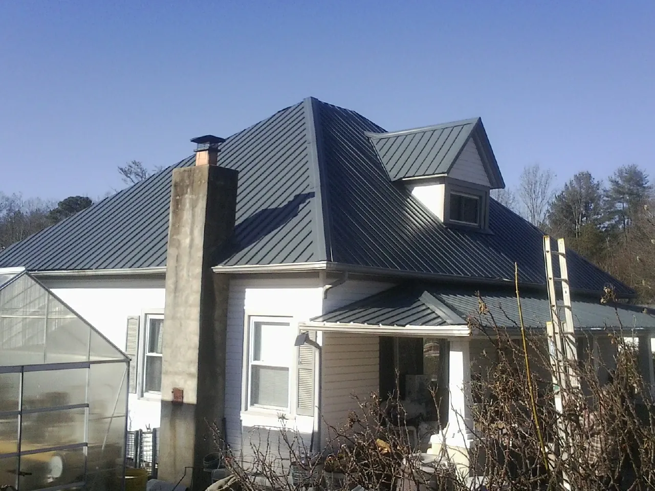 Dark blue standing seam metal roof on a white farmhouse with dormer — Slate & Tile Roof Repair by Roofing Brothers in Nielsville