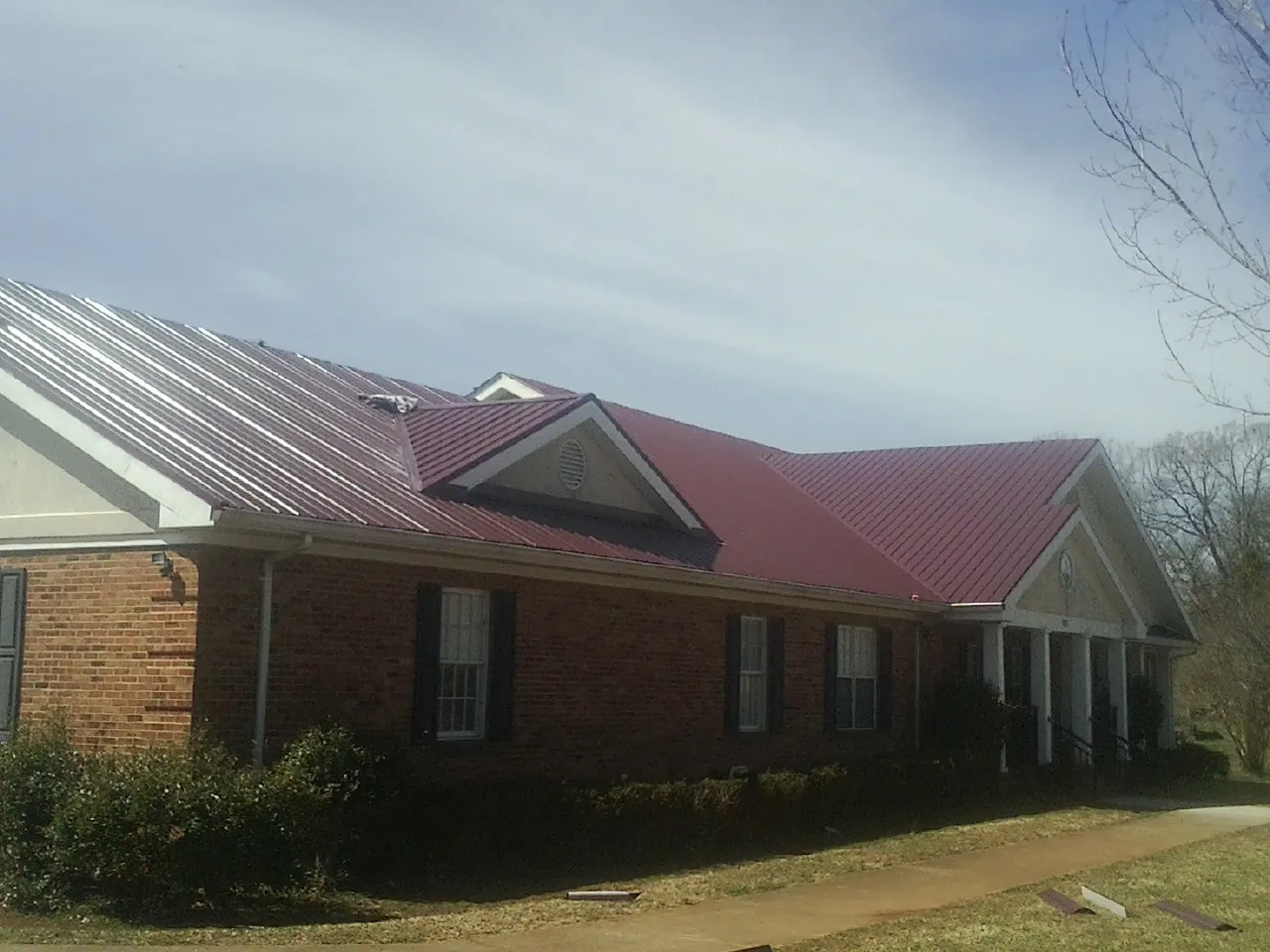 Red metal roof with gabled entries on a long brick building, from a Hail Damage Roof Repair job in Nielsville