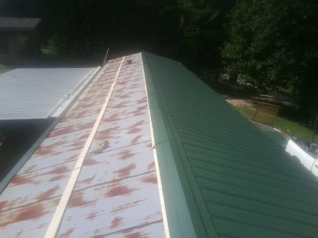 Old rusted panels beside newly installed green metal roofing — Wind Damage Roof Repair by Roofing Brothers in Nielsville