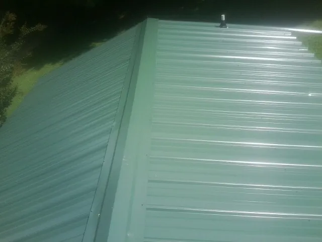 New green metal panels meeting at the ridge of a roof — Flat Roof Repair work by our crew in Nielsville