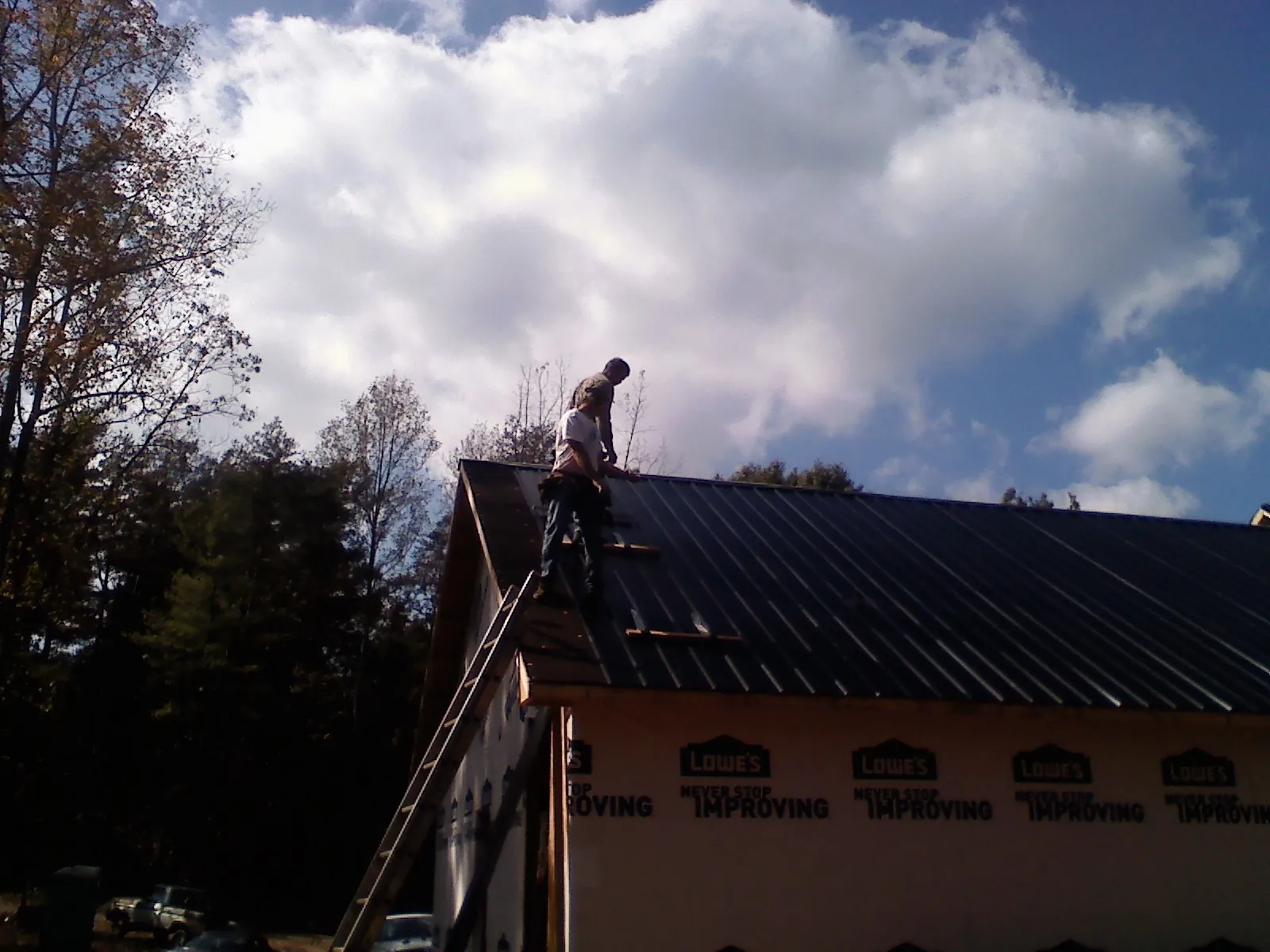 Roofer fastening dark metal panels high against a cloudy sky, from a Roof Inspection job in Nielsville