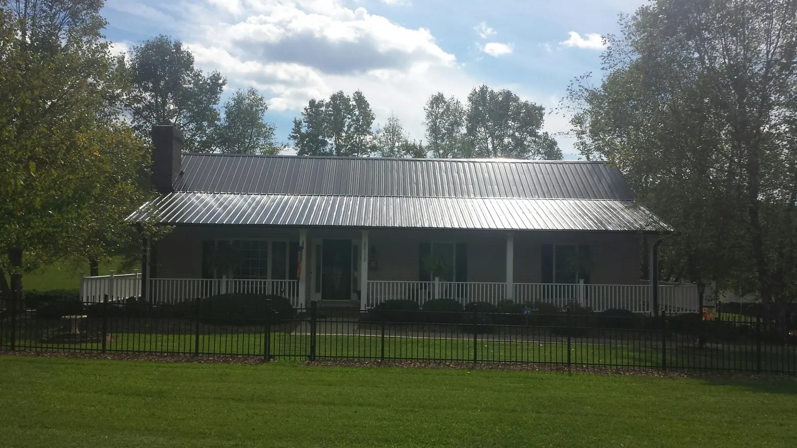 Gray metal roof on a brick ranch with a full width front porch — Gutter Guard Installation work by our crew in Nielsville
