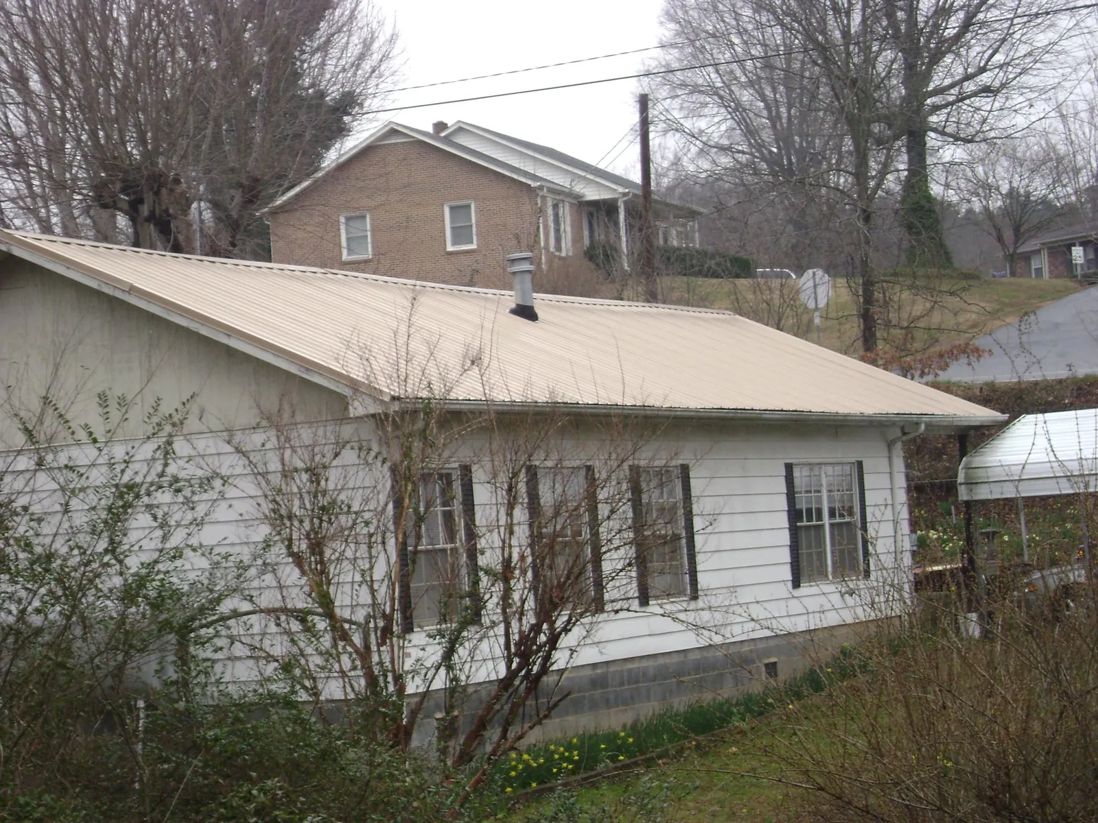 Tan metal roof on a white sided house set into a hillside — Commercial Roofing by Roofing Brothers in Nielsville