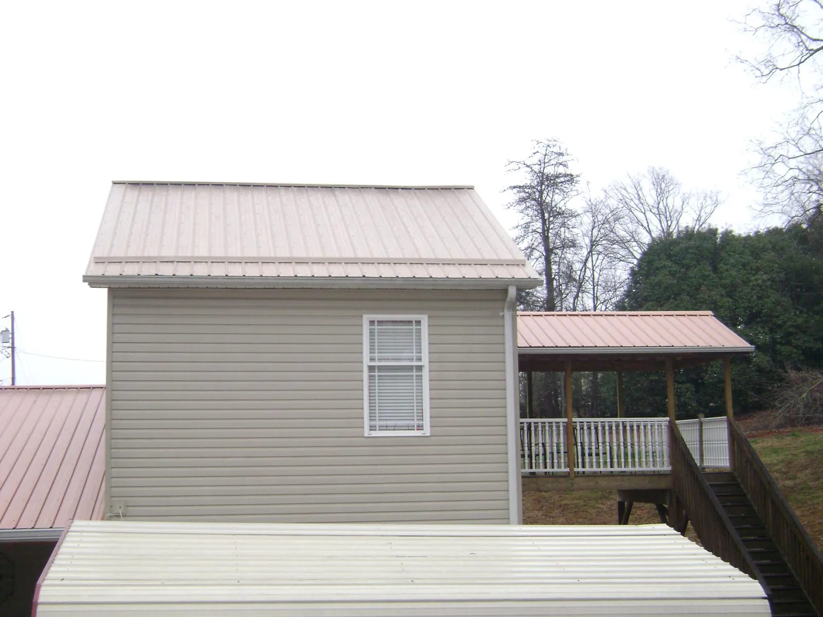 Tan metal roofs on a two story addition and attached porch, from a Roof Replacement job in Nielsville